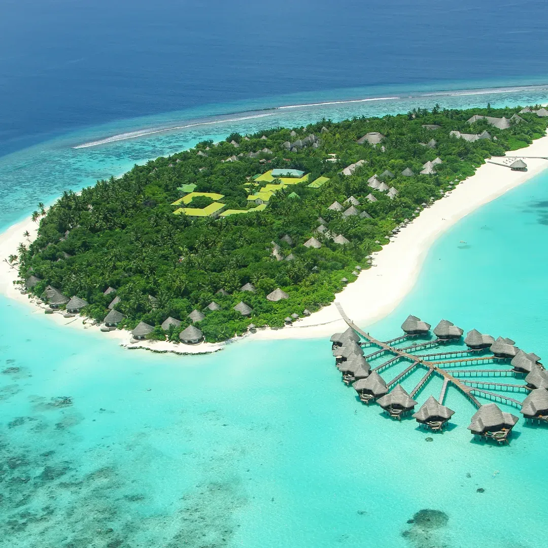Aerial view of a lush Maldives resort island with thatched beach villas, water villas fanning out over a bright turquoise lagoon
